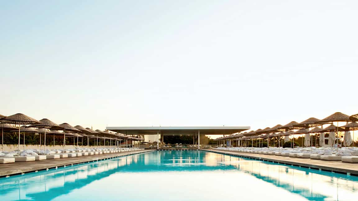 En stor og lang pool med parasoller og liggestole på begge sider. (AI-genereret tekst)