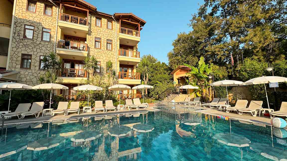 Billede af hotelfacade med pool og liggestole foran. (AI-genereret tekst)