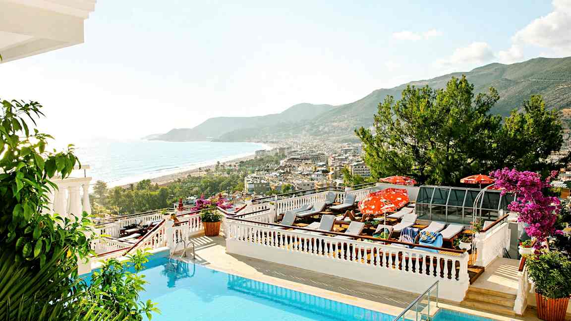 Udsigt over en pool med liggestole, havet og en kystby i baggrunden. (AI-genereret tekst)