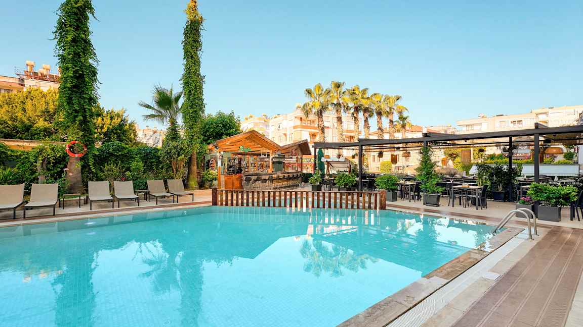 Udendørs pool med liggestole, træer og en bar i baggrunden. (AI-genereret tekst)