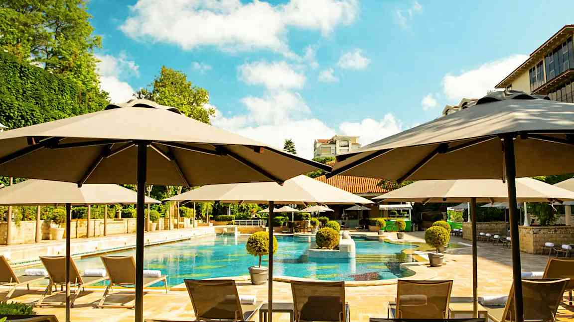 Poolområde med parasoller, liggestole og omgivende beplantning. (AI-genereret tekst)