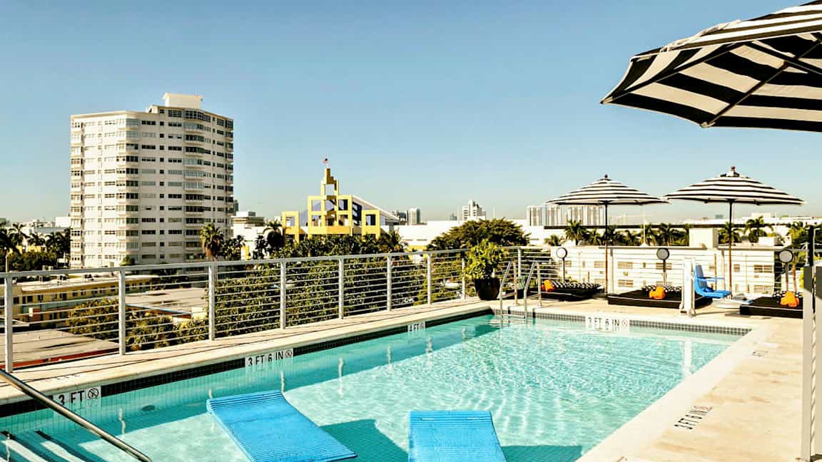 En tagpool omgivet af stribede parasoller med udsigt til byen og flere bygninger i baggrunden. (AI-genereret tekst)