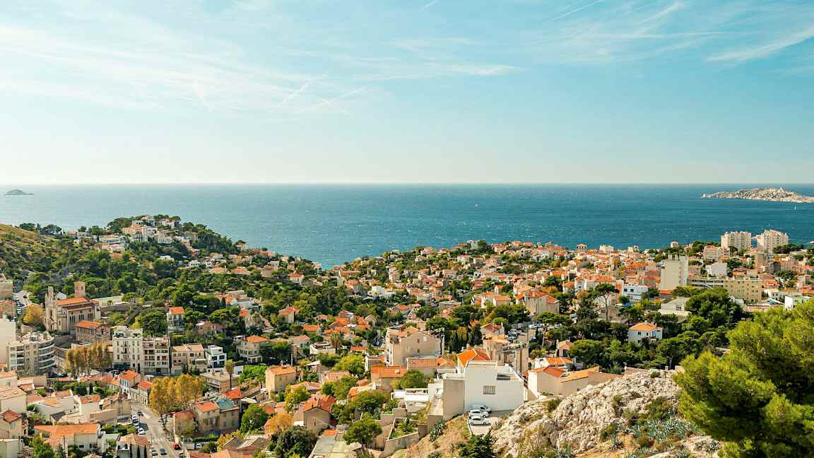 Udsigt over en kystby med røde tage og grøntområder samt havet i baggrunden. (AI-genereret tekst)