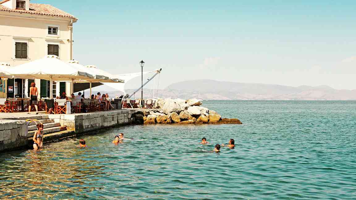 Folk svømmer i havet nær en café ved stranden. (AI-genereret tekst)