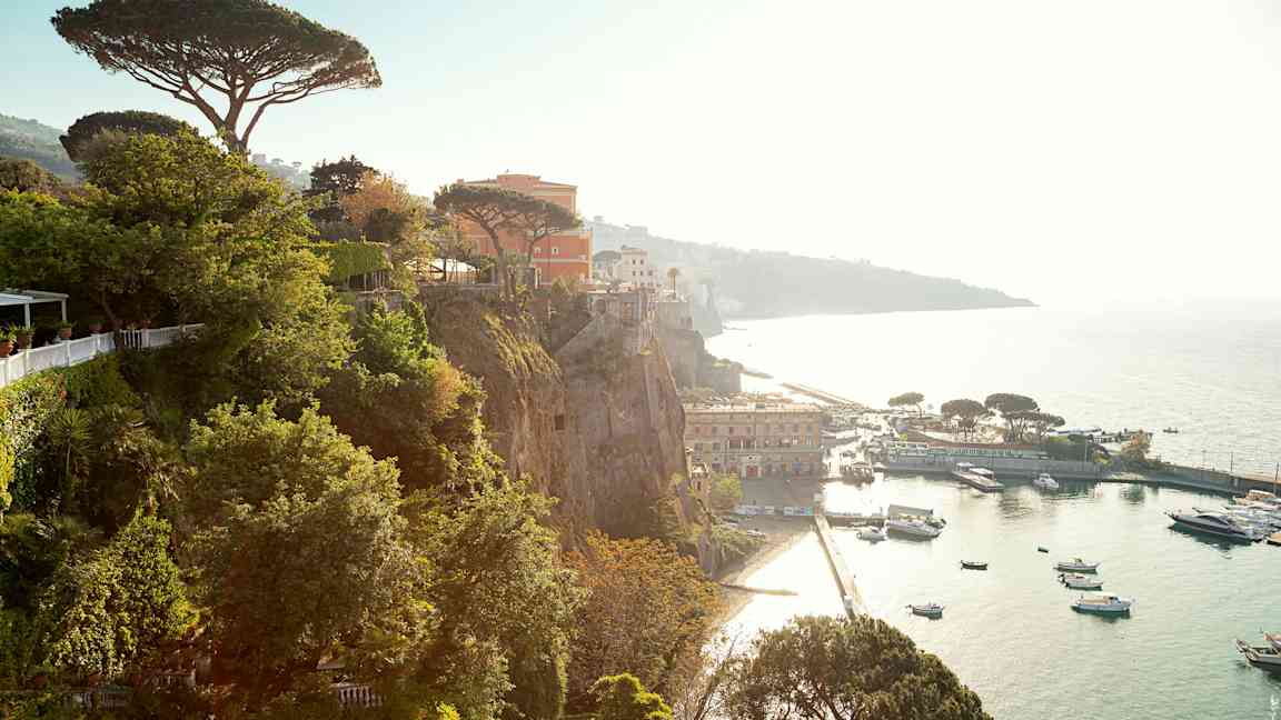 Udsigt fra klippe over havn med både og bygninger. (AI-genereret tekst)