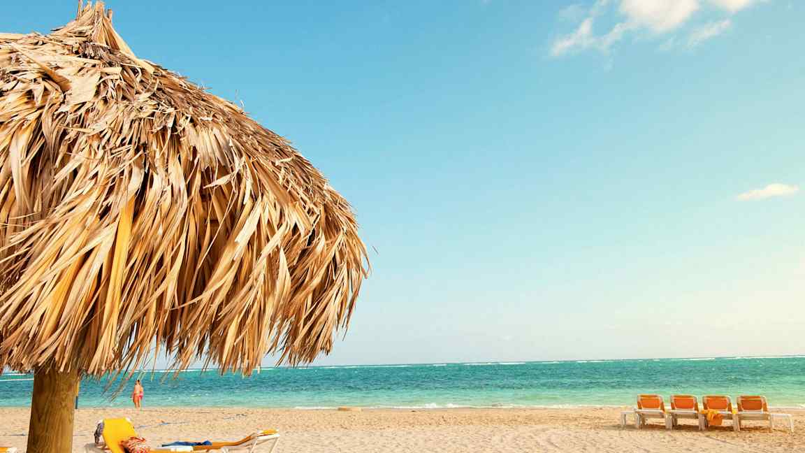 En strand med liggestole og en parasol af tørrede palmeblade. (AI-genereret tekst)