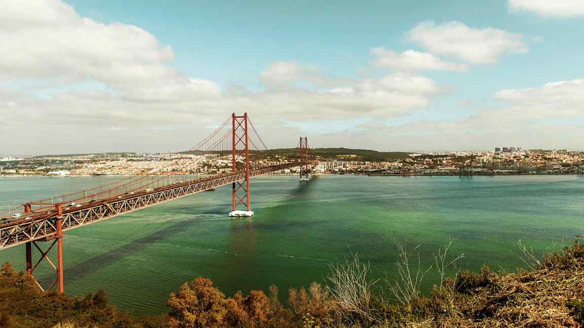 Billedet viser en rød bro over vand med en by i baggrunden. (AI-genereret tekst)