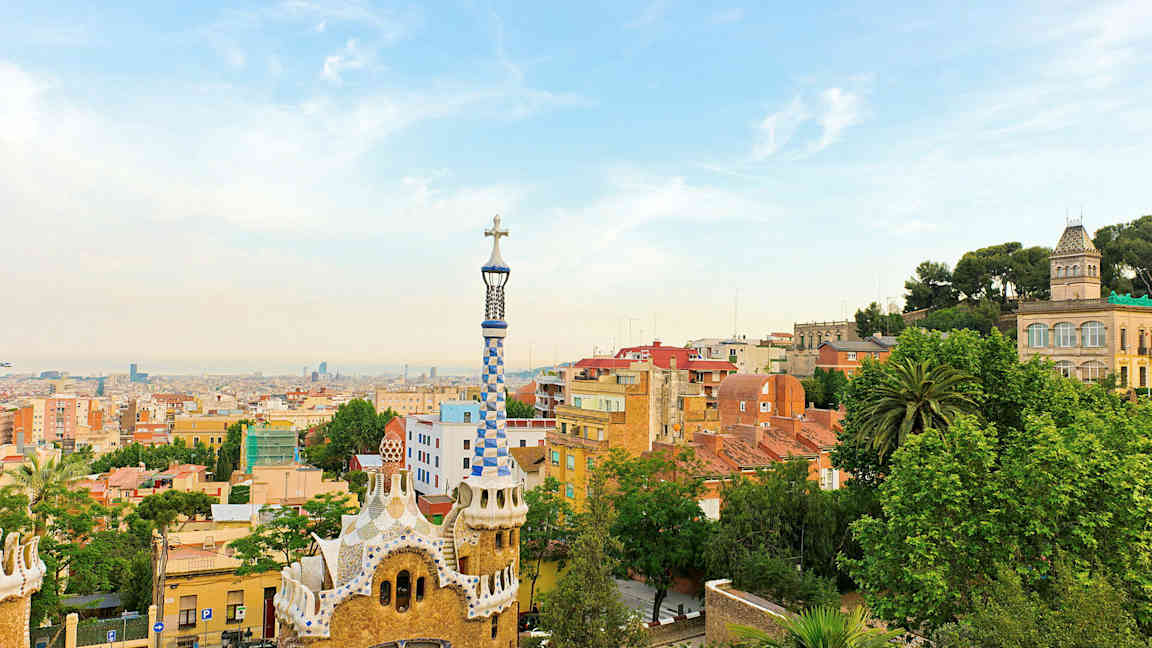 Udsigt over Park Güell i Barcelona med farverige bygninger og byens skyline i baggrunden. (AI-genereret tekst)