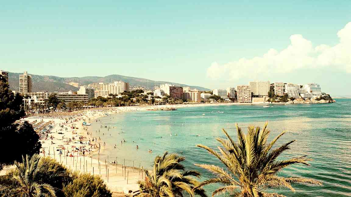 En strand ved havet omgivet af bygninger og palmer. (AI-genereret tekst)