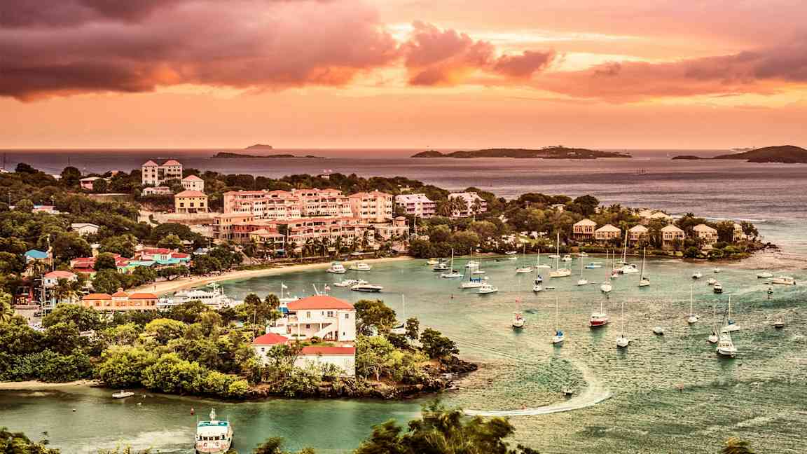 Billede af en kystby med både ved en marina, omgivet af grønne træer og solnedgang i baggrunden. (AI-genereret tekst)