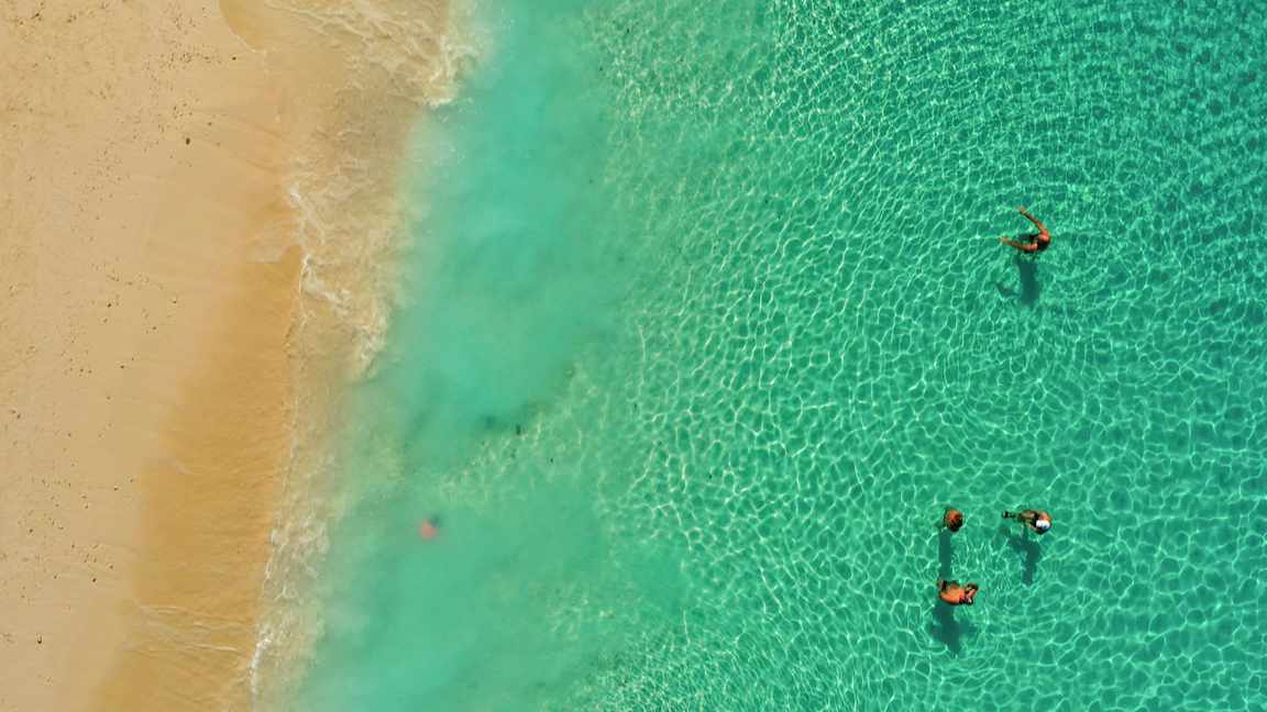 Luftfoto af personer, der svømmer i havet nær en sandstrand. (AI-genereret tekst)