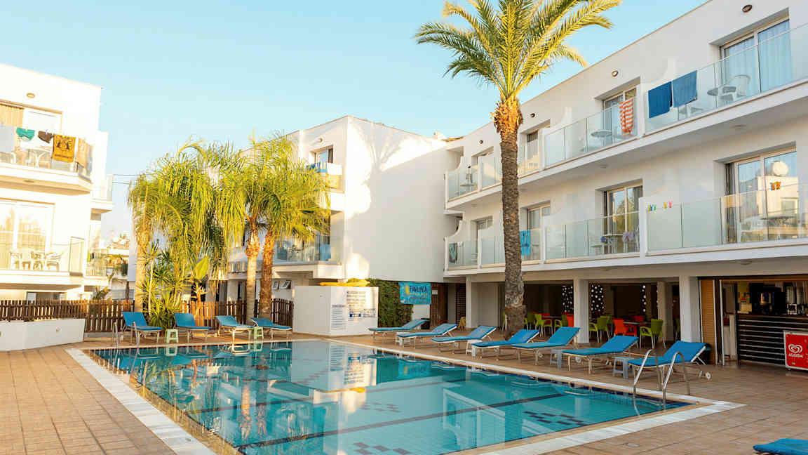 En udendørs pool omgivet af liggestole og hvide bygninger. (AI-genereret tekst)