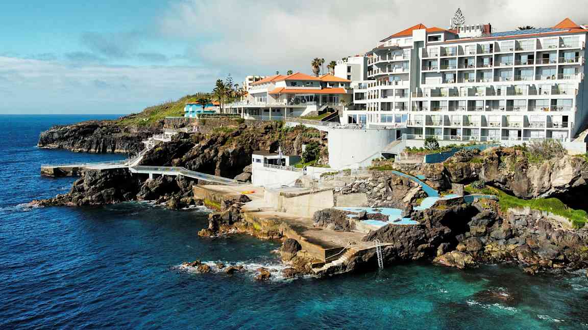 Hotelbygninger ved klipper med udsigt over havet og poolområder. (AI-genereret tekst)