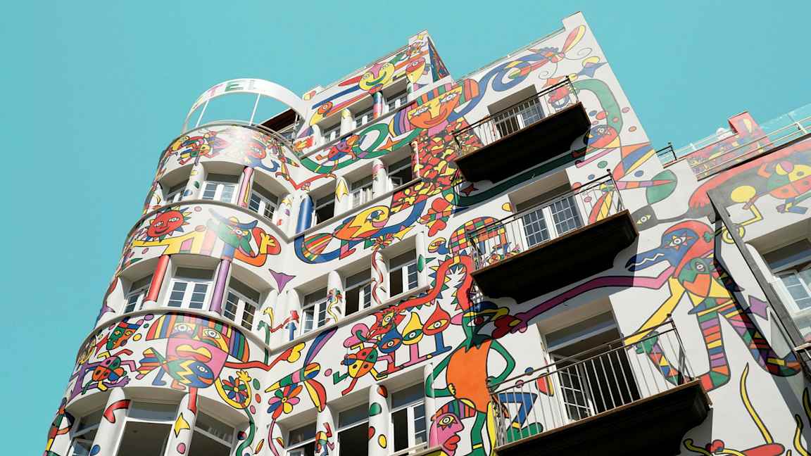 Bygning med farverige abstrakte malerier på facaden mod en klar blå himmel. (AI-genereret tekst)