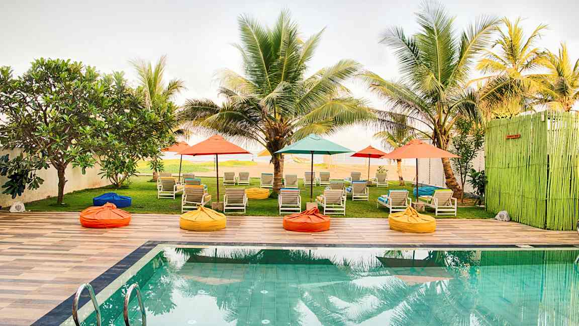 En pool med liggestole og farverige parasoller i en have omgivet af palmer. (AI-genereret tekst)