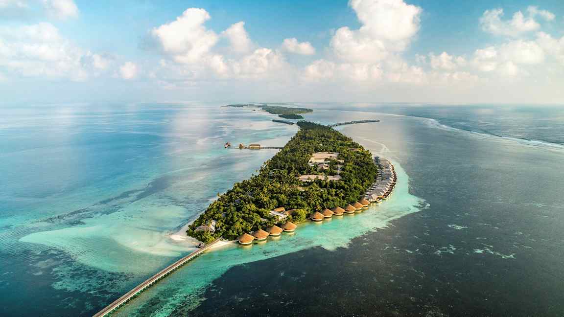 Luftfoto af en tropisk ø med villaer over vandet og turkis hav. (AI-genereret tekst)