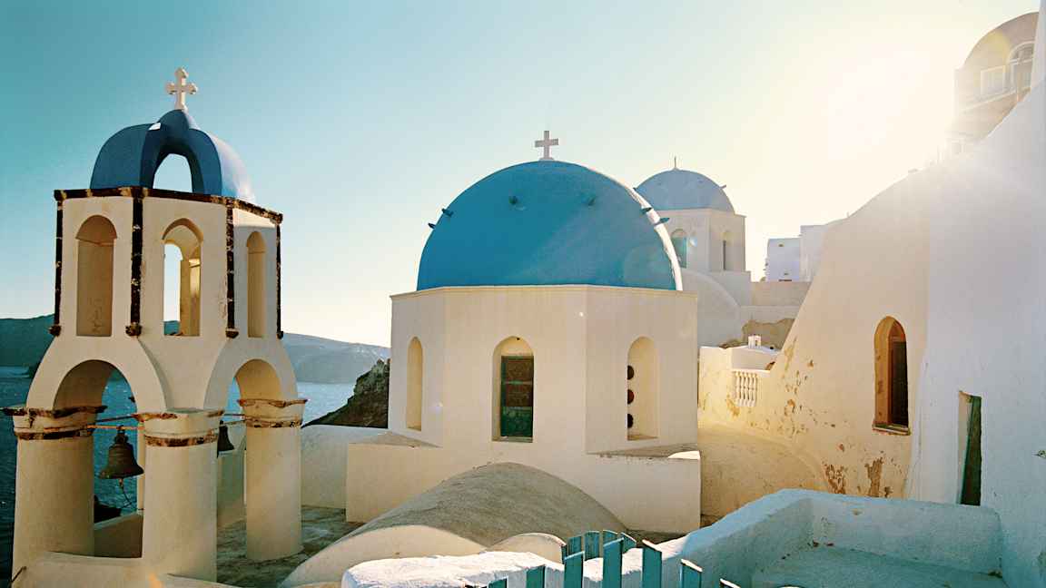 En hvid bygning med blå kuppel og klokketårn i solrigt landskab. (AI-genereret tekst)