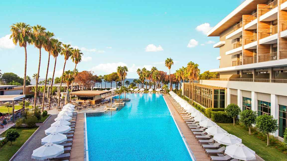 Et hotel med pool og liggestole omgivet af palmer. (AI-genereret tekst)