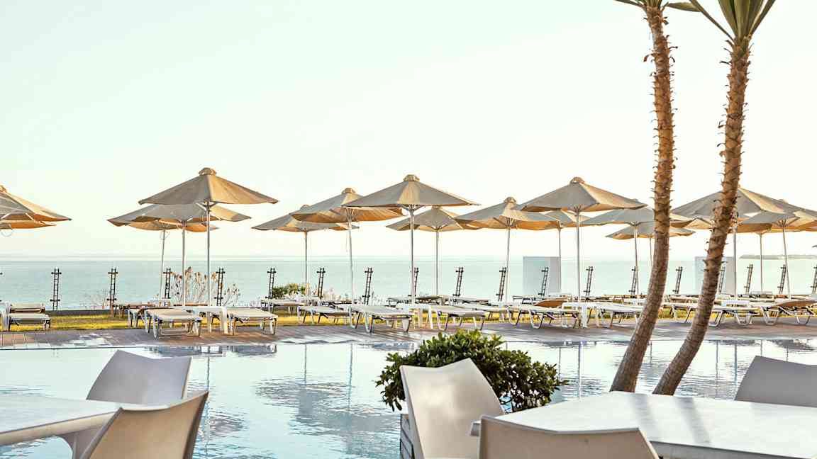 Solterrasse ved poolen med liggestole og parasoller ved havet. (AI-genereret tekst)