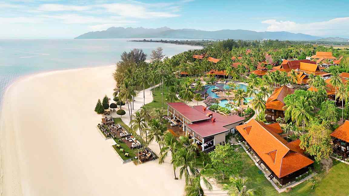 Strand med hvid sand ved siden af frodig resort med orange tage og poolområde. (AI-genereret tekst)