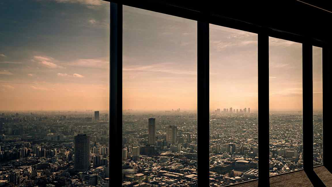 Udsigt over en by gennem høje vinduer med solnedgang i baggrunden. (AI-genereret tekst)