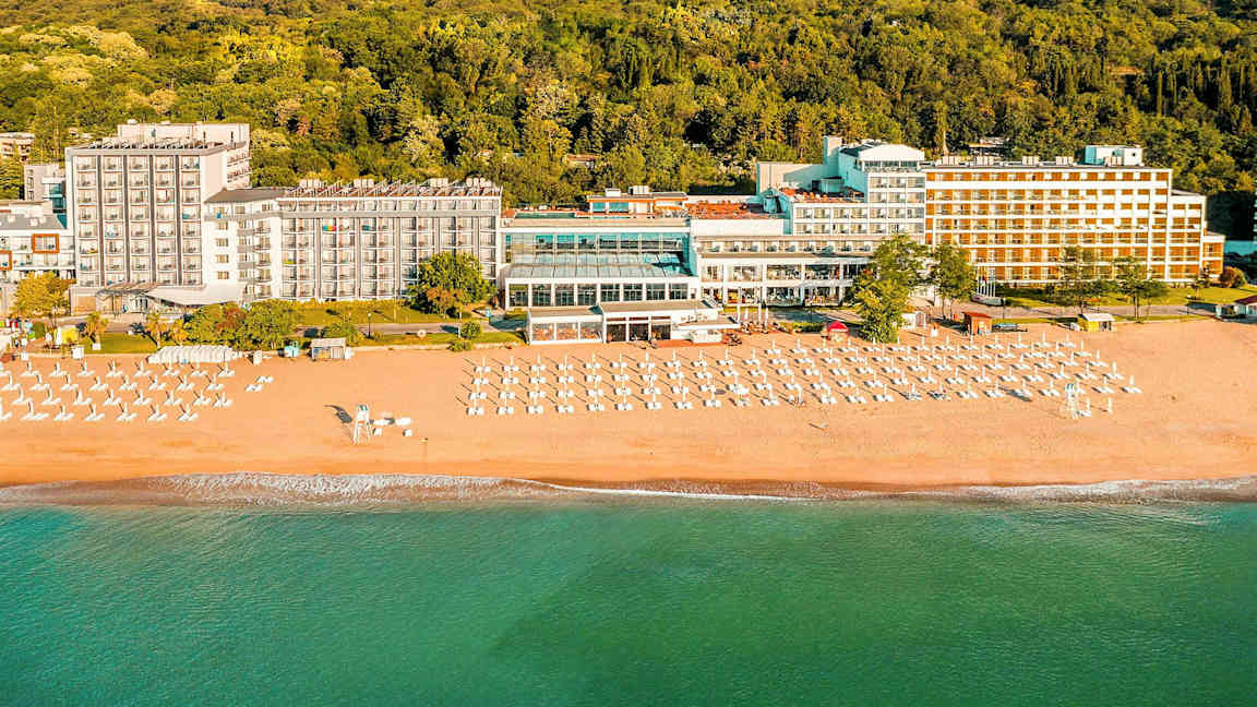 Hotel ved stranden med liggestole og parasoller foran en skov. (AI-genereret tekst)
