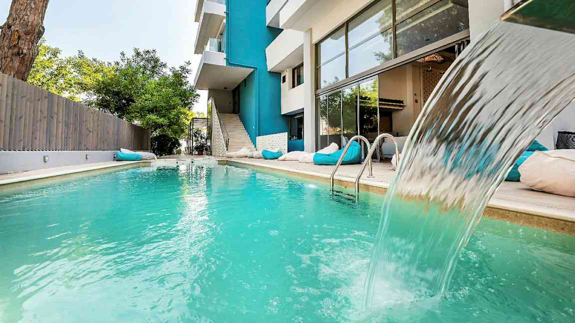 Udendørs swimmingpool med vandfald ved siden af en moderne bygning. (AI-genereret tekst)