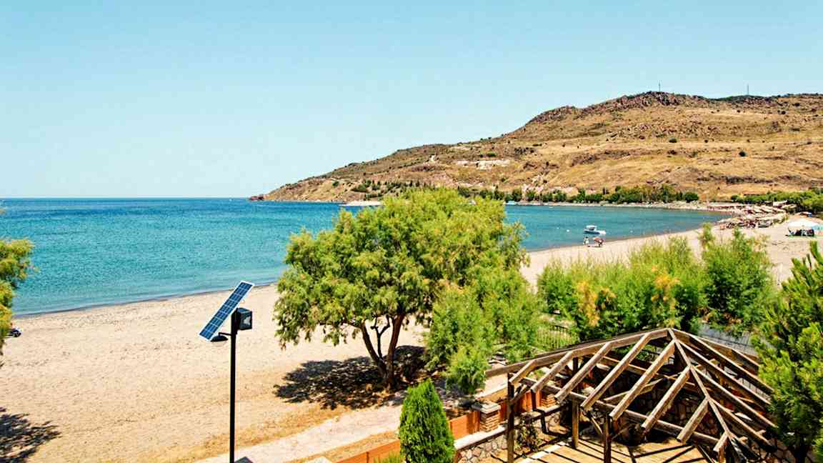 En strand med klart blåt hav, omgivende grønt og en trækonstruktion i forgrunden. (AI-genereret tekst)