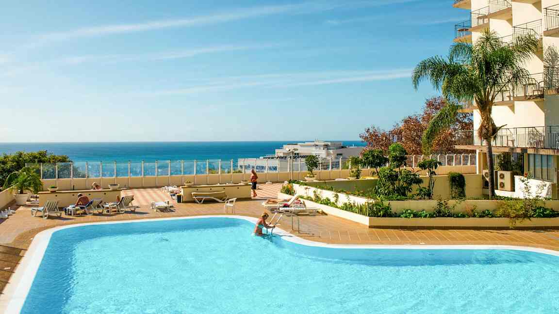 En udendørs swimmingpool med liggestole og en klar blå himmel over havet. (AI-genereret tekst)