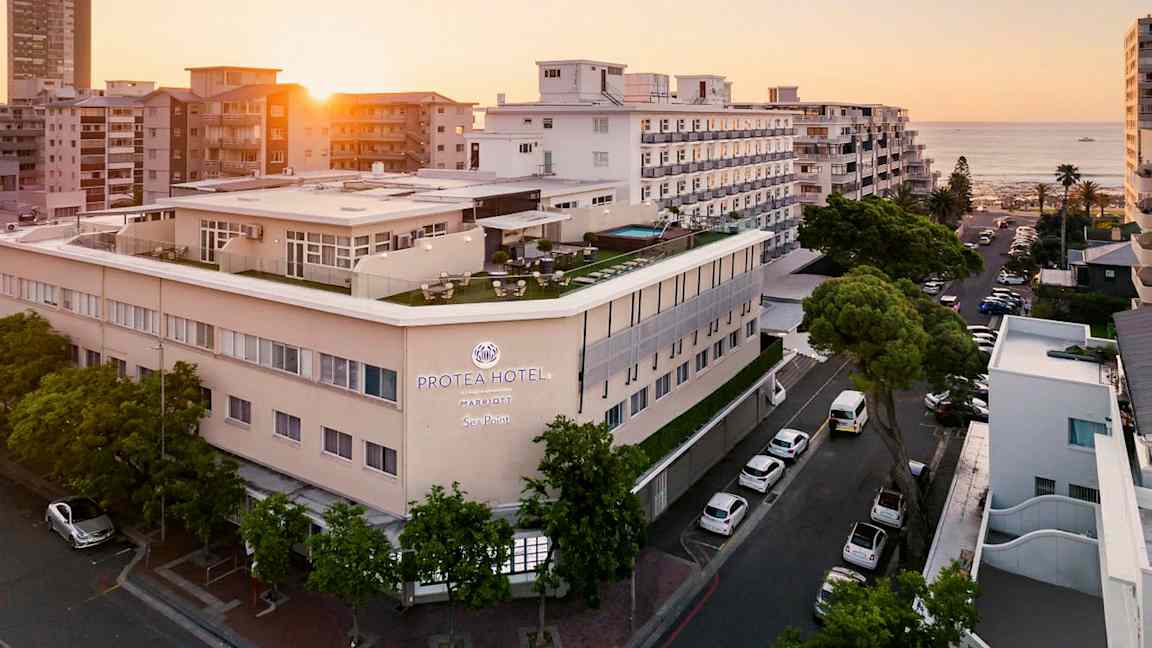 Hotelbygning ved havet omgivet af andre bygninger i solnedgang. (AI-genereret tekst)