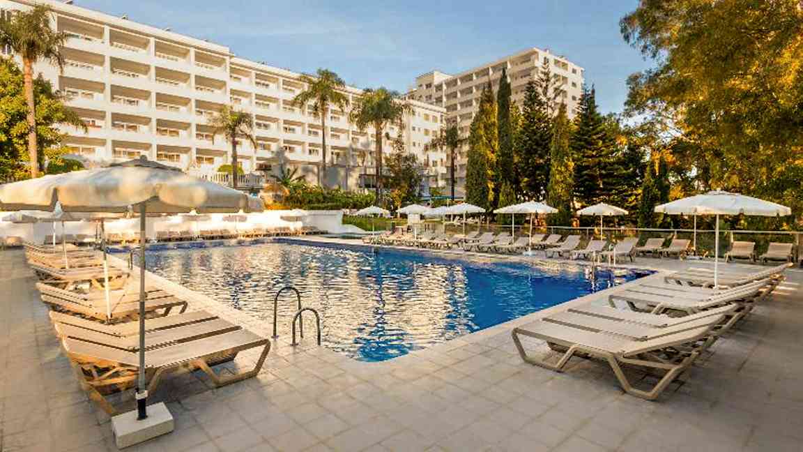 Billede af en udendørs swimmingpool ved et hotel omgivet af liggestole og parasoller. (AI-genereret tekst)
