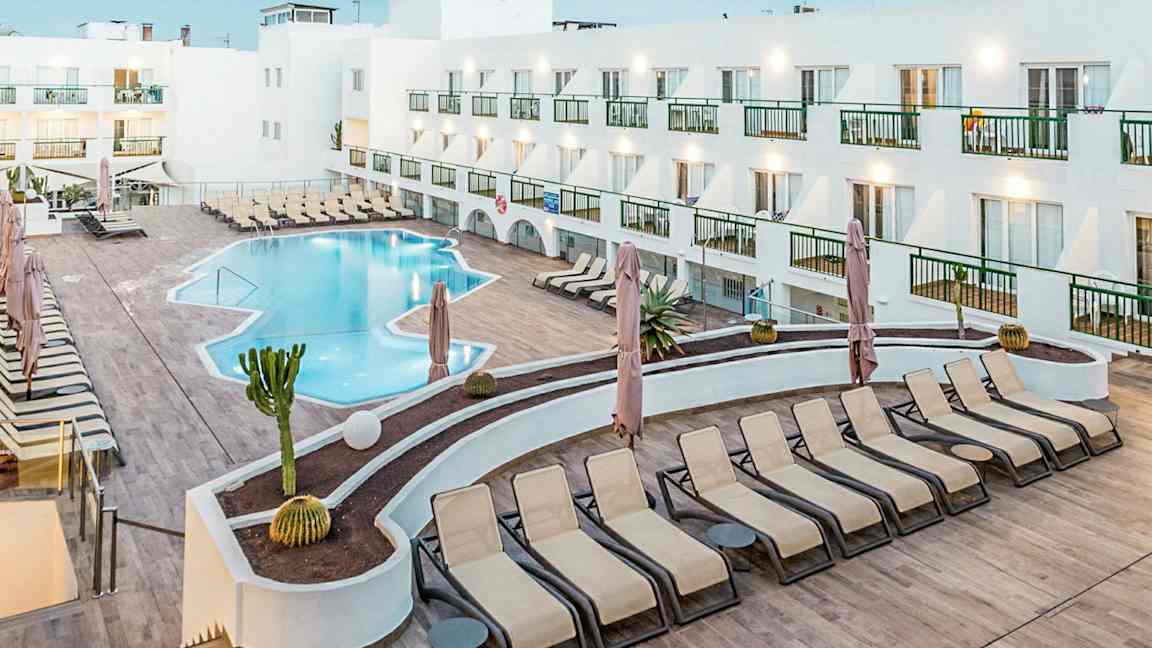 En hotelpool med liggestole og en hvid bygning omkring. (AI-genereret tekst)