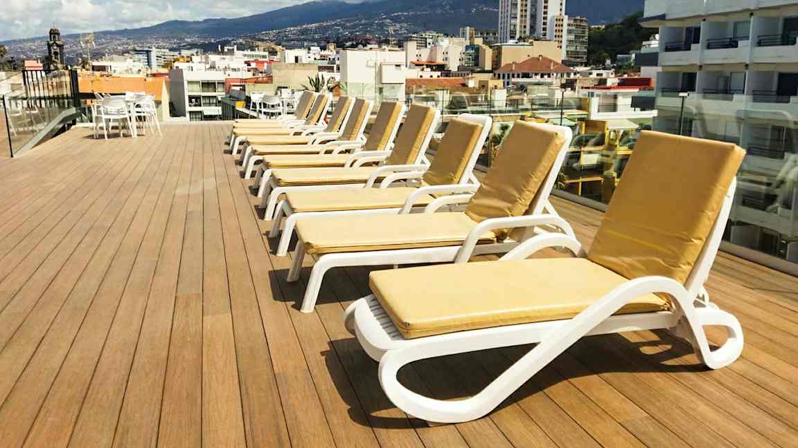 En tagterrasse med liggestole og udsigt over en by og omkringliggende bjerge. (AI-genereret tekst)