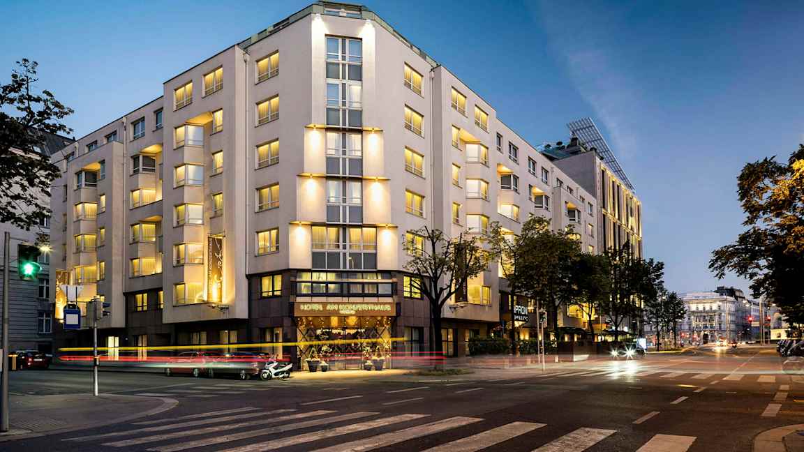 En bygning oplyst om aftenen, med flere etager og vinduer, beliggende ved et vejkryds. (AI-genereret tekst)