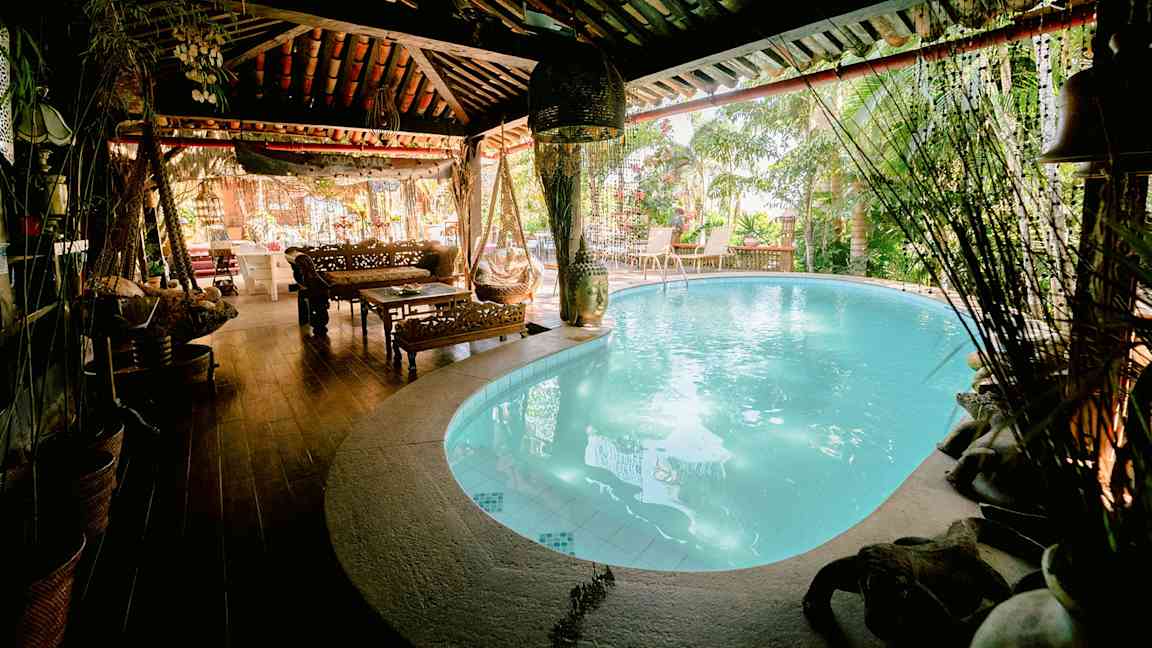 Et hyggeligt område med en indendørs pool, træmøbler og planter omkring. (AI-genereret tekst)