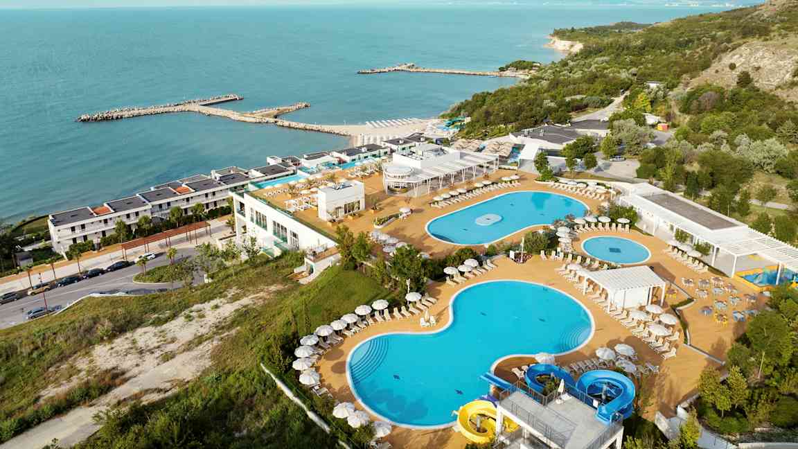 Billede af en ferieresort ved havet med pools, liggestole og frodige omgivelser. (AI-genereret tekst)
