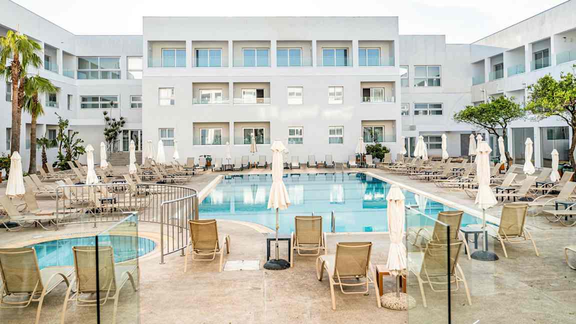 Et hotel med en udendørs pool og liggestole, omgivet af hvide bygninger. (AI-genereret tekst)