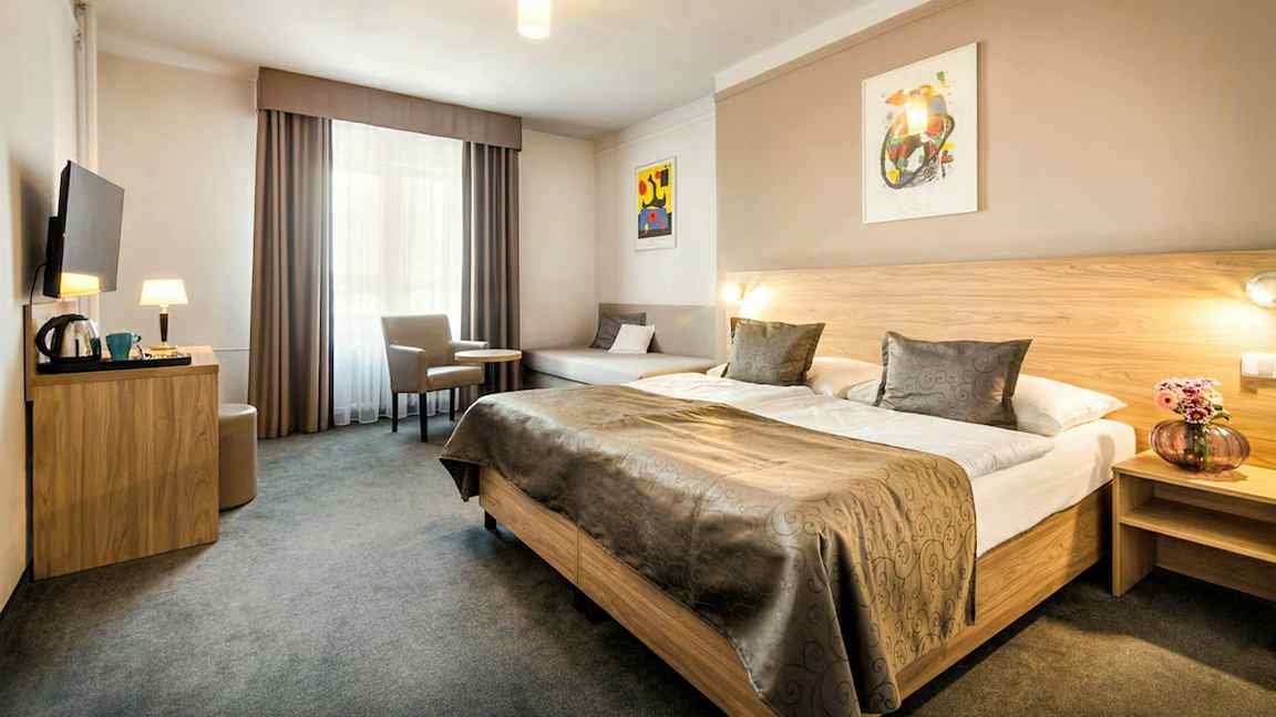 Et hotelværelse med en stor dobbeltseng, et bord med to stole og et vægmonteret TV. (AI-genereret tekst)