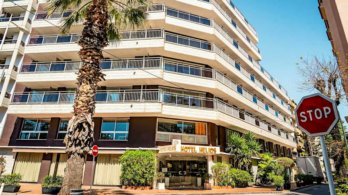 Et hotel med flere etager og et palmetræ foran. Skiltet "STOP" er synligt til højre. (AI-genereret tekst)