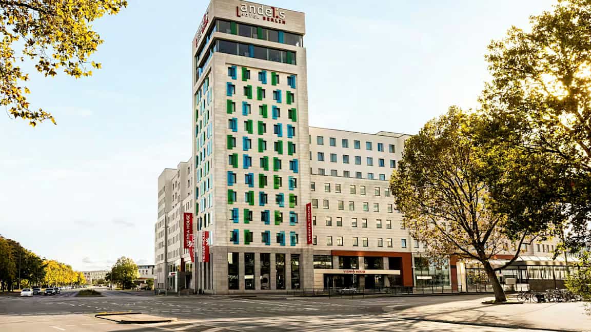 En moderne hotelbygning med hvid facade og farvede vinduer, omgivet af veje og træer. (AI-genereret tekst)