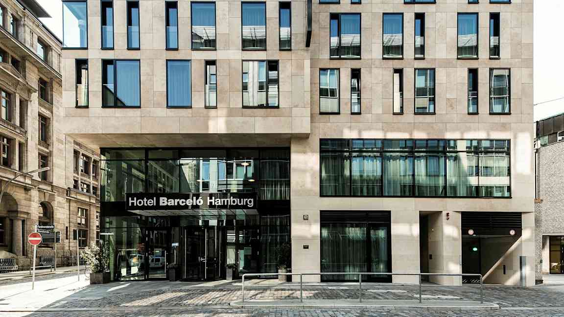 En bygning med en moderne facade og en indgang med teksten "Hotel Barceló Hamburg". (AI-genereret tekst)