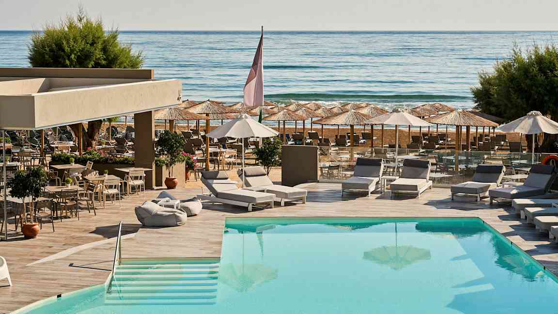 Udendørs pool med liggestole og parasoller, samt udsigt mod havet. (AI-genereret tekst)