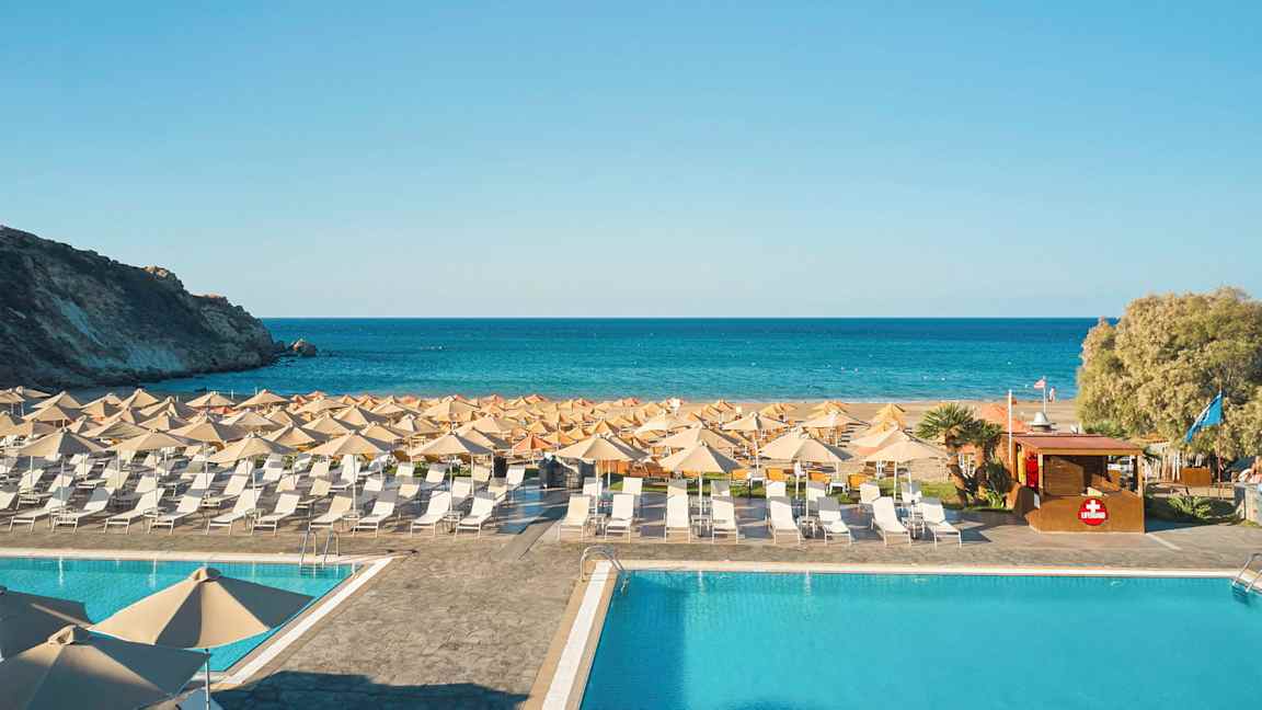 En pool foran en strand med liggestole og parasoller, og havet i baggrunden. (AI-genereret tekst)