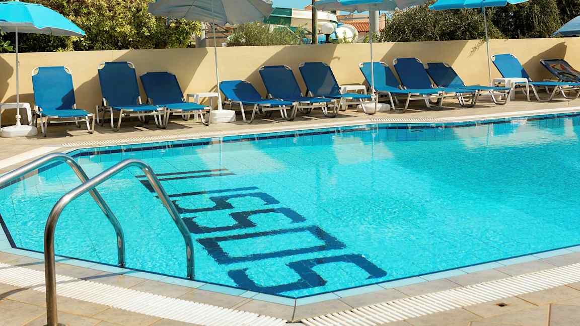 En udendørs pool med blå liggestole og parasoller langs kanten. (AI-genereret tekst)