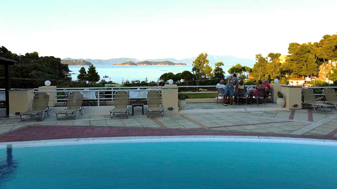 Udsigt fra en poolterrasse med liggestole, med hav og øer i baggrunden. (AI-genereret tekst)