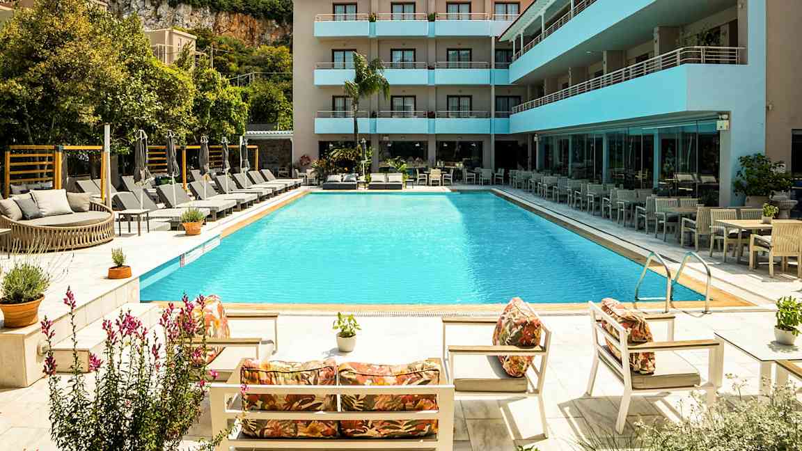 En udendørs pool omgivet af liggestole og parasoller ved et moderne hotel. (AI-genereret tekst)