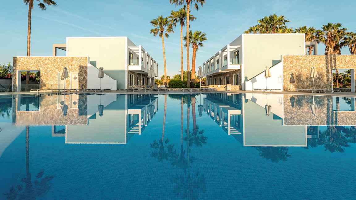 To moderne bygninger ved en pool med palmer i baggrunden. (AI-genereret tekst)