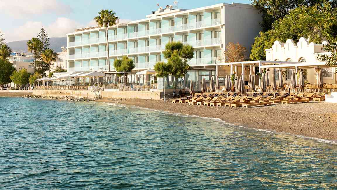 Udsigt til et strandhotel med liggestole og parasoller på stranden og havet i forgrunden. (AI-genereret tekst)