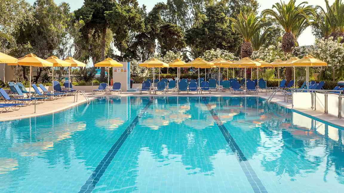 Udendørs swimmingpool med blåt vand, omgivet af liggestole, parasoller og grønne træer. (AI-genereret tekst)