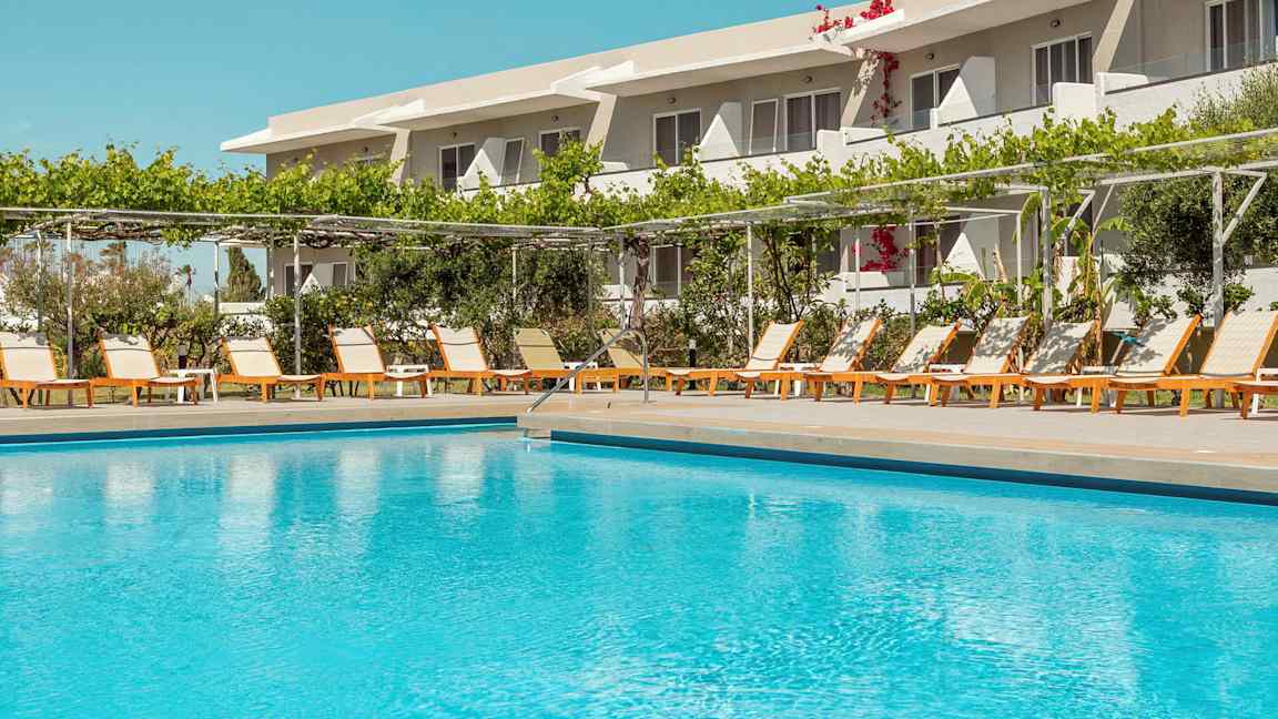 Udendørs pool foran en række liggestole og et hotel i baggrunden. (AI-genereret tekst)